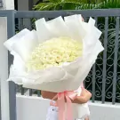 A large bouquet of white roses wrapped in white paper, tied with a pink ribbon.