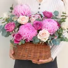 Pink and purple flowers in a woven basket, held by a person.