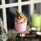 Chocolate cupcake with cherry, walnut, and chocolate stick topping in a pink polka-dot wrapper.