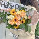 A bouquet of yellow gerbera daisies, peach roses, and pink carnations wrapped in newspaper.