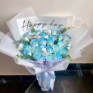 A bouquet of blue and white roses with a "Happy day" tag, tied with a light blue ribbon.