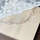 Silver chain bracelet with rose quartz beads and small floral charms.