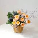 Basket of peach David Austin roses and blue thistles, tied with twine.