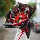 Bouquet of red roses and carnations with eucalyptus leaves, wrapped in dark brown and red paper.