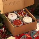 Christmas gift box with four scented candles featuring Santa, reindeer, and festive patterns.