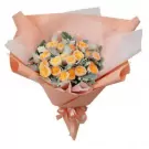 Bouquet of yellow and orange roses with grey-green foliage, wrapped in peach paper and tied with a peach ribbon.