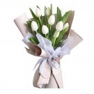 A bouquet of white tulips with green leaves, wrapped in brown and white paper, tied with a white ribbon.