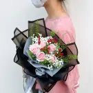 Bouquet of pink roses, baby's breath, and red berries with black and gray wrapping.