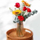 Red roses and sunflowers in a tall glass vase on a woven tray.
