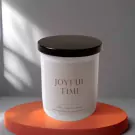 A white candle with "JOYFUL TIME" printed on it, on an orange pedestal.