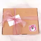 A brown gift box with a pink ribbon and bow, a white tag, and a Lotso bear sticker.