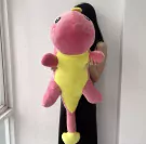 A person holds a large pink and yellow plush dinosaur toy.