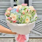 A bouquet of pink, white, and blue hydrangeas and roses wrapped in white paper with a pink ribbon.