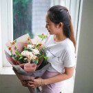 Woman in white t-shirt holding a bouquet of pink roses, green leaves, and small red berries.