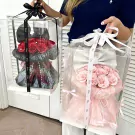 Two clear boxes hold floral bunny arrangements: one with red roses and a black bow, the other with pink roses and a white bow.