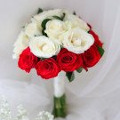 Bridal bouquet of red and white roses with a white ribbon stem, with tiny white flowers below.