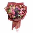 A lush bouquet of pink and purple flowers wrapped in deep red paper and tied with a ribbon.