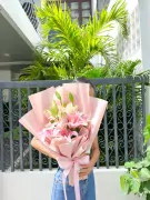Pink lilies bouquet in light pink paper with a pink ribbon tied around the stems.