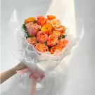 Bouquet of orange and pink roses with white lace and pink ribbon.