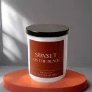 White candle with "Sunset On The Beach" label on an orange stand.