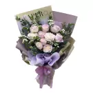Bouquet of white and pink roses with eucalyptus and purple paper wrap, tied with a purple ribbon.