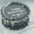 Dark gray birthday cake with white lettering and frosting decorations.