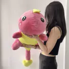 A person holds a large, plush pink dinosaur with a yellow belly and feet.