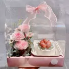 Floral gift box with pink roses, greenery, and a small cake topped with strawberries.