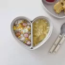 Heart-shaped lunchbox with rice, corn, sausage, and soup.