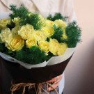 Yellow roses and carnations with green foliage in a rustic bouquet.
