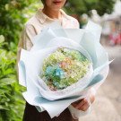 Woman holding a pastel bouquet of hydrangeas wrapped in light blue and white paper.