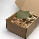 Cardboard gift box with shredded paper, dried flowers, and a green card.