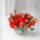 Red and orange flowers in a clear glass vase with berries and greenery.