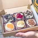 Six assorted vanilla brownies topped with cookies, cherry, chocolate, caramel, and nuts.
