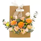 Gift bag with orange roses, lisianthus, and accent flowers, tied with white ribbon.