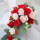 Red and pale pink roses with red berries and eucalyptus leaves in a cascading bouquet.
