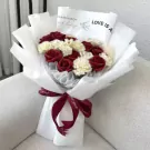 Red and white flowers in a bouquet wrapped in white paper, tied with a dark red ribbon.