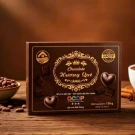 Brown box of Le Chocolatier chocolate with heart-shaped chocolates and cocoa beans.