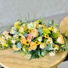 Bright floral arrangement with roses, sunflowers, and greenery on a wooden table.