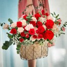 A hand holding a basket of red and pink roses with greenery.