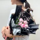 A bouquet of pink roses with black and gold wrapping.