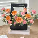 Orange and pink roses, carnations, and daisies in a black floral box.