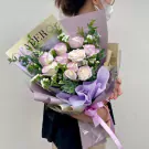 A person holds a bouquet of light purple and white roses with eucalyptus leaves.