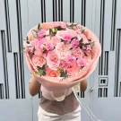 Pink roses and carnations in a soft pink bouquet with ribbon accents.