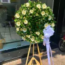 White gerbera daisies and baby's breath wreath on a wooden easel with a white ribbon.