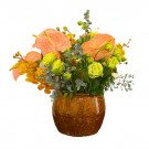 Pink anthuriums, yellow orchids, and green ranunculus in a brown ceramic vase.