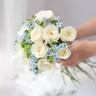 White roses and blue flowers in a bridal bouquet held by hands.