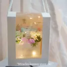 A gift box with a scented candle and flowers, decorated with fairy lights.