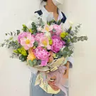 A woman holds a bouquet of pink peonies, tulips, and carnations with eucalyptus leaves.