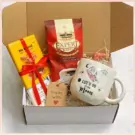 Gift box with coffee, yellow item, mug with cartoon drawing, and tag.
